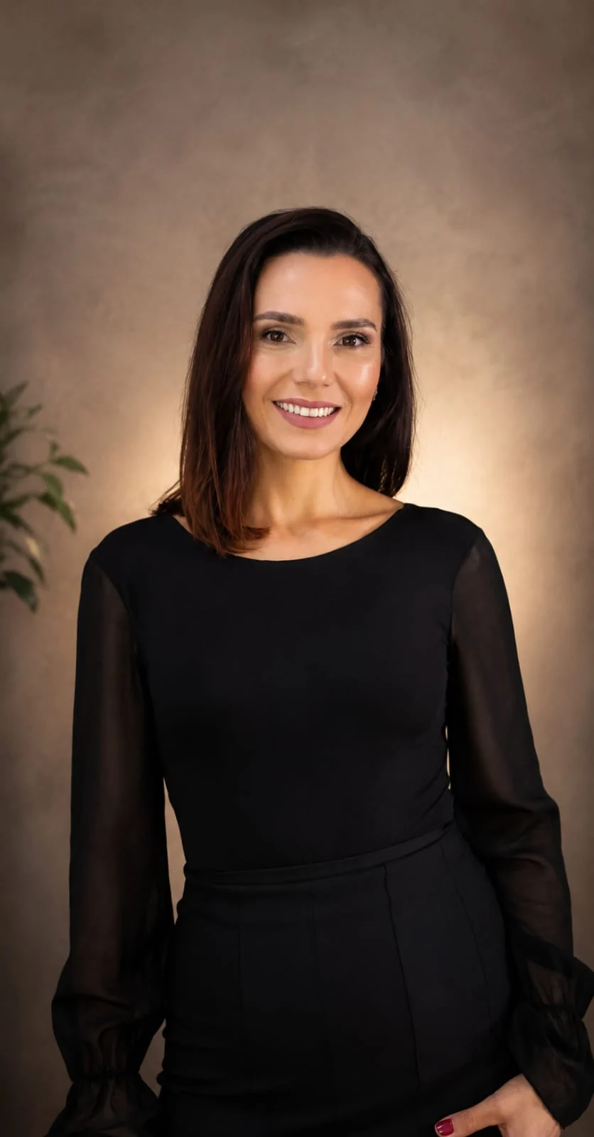 Patrícia sorrindo, de roupa preta, em um fundo bege iluminado